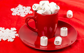 Красная чашка с маршмеллоу на столе со снежинками