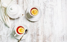 Две чашки чая с лимоном на столе с белым чайником