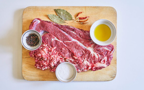 Кусок мяса со специями и оливковым маслом на доске 