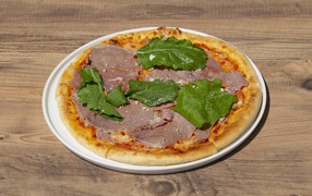 Пицца с кусочками мяса и зеленью на столе