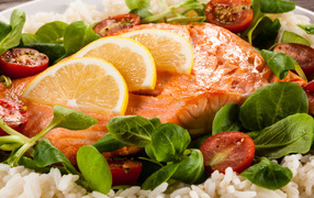 Кусок запеченной красной рыбы на тарелке с лимоном, рисом, базиликом и помидорами