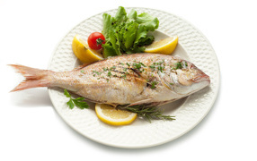 Запеченная рыба на тарелке с зеленью и лимоном