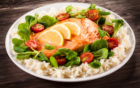 Piece of fish on a plate with tomatoes, rice and basil leaves