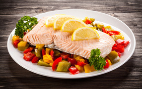 Кусок рыбы на тарелке с овощами и лимоном