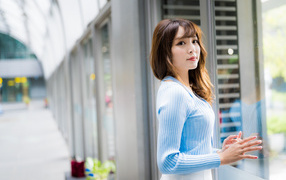 Красивая девушка азиатка в в голубой кофте стоит уокна