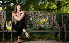 Девушка в черном костюме сидит на лавке 