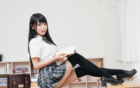 Девушка азиатка в костюме школьницы на парте 