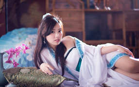 Девушка азиатка в красивом платье лежит на кровати 