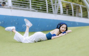 Девушка азиатка в наушниках лежит на полу 