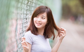Девушка азиатка с милой улыбкой стоит у сетки 