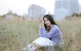 Красивая девушка азиатка сидит на поле с травой 
