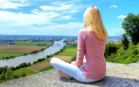 Красивая блондинка сидит на камне у реки