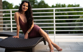 Красивая брюнетка в платье сидит на диване 