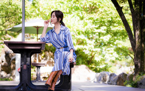 Красивая девушка в платье сидит за столиком в парке