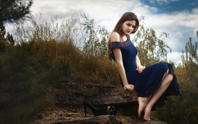 Beautiful girl in a long blue dress sits on a stone