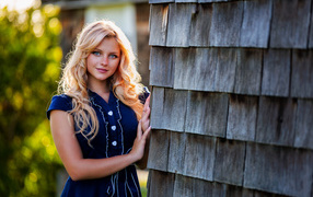 Голубоглазая блондинка в платье стоит у стены 