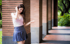 Cute Asian girl in a skirt stands at the column
