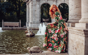 Девушка в красивом цветастом платье у пруда в парке 