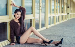 Девушка в свитере сидит у стеклянной стены 