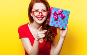 Девушка в очках с подарком в руке на желтом фоне