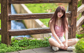 Длинноволосая азиатка сидит у забора 