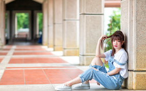 Грустная девушка азиатка сидит у колонны