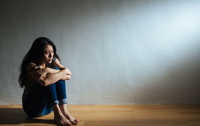 Испуганная девушка азиатка сидит у стены