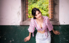 Улыбающаяся девушка азиатка стоит у окна 