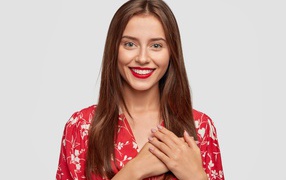 Улыбающаяся девушка с руками на сердце на сером фоне