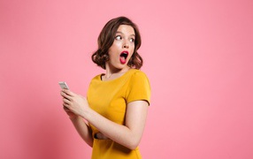 Удивленная девушка с телефоном в руках на розовом фоне