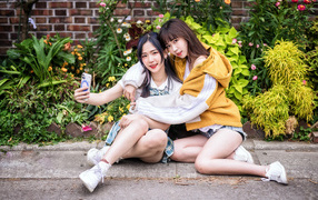Две девушки азиатки сидят у стены с цветами 
