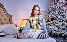 Милая девушка на кровати у новогодней елки 