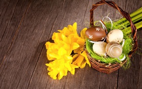 Basket with colored Easter eggs on the table with a bouquet of daffodils