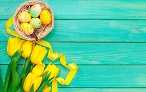 Multicolored easter eggs and a bouquet of yellow tulips on a blue background