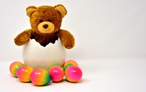 Медвежонок с яркими пасхальными яйцами на сером фоне