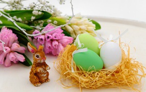 Три пасхальных яйца в гнезде на столе с цветами