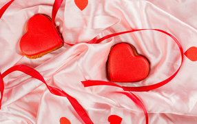 Два красных сердечка с ленточкой на розовой ткани на день влюбленных