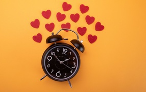 Black alarm clock with hearts on orange background
