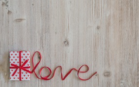 Коробка с подарком  и надпись любовь красной лентой на деревянном фоне