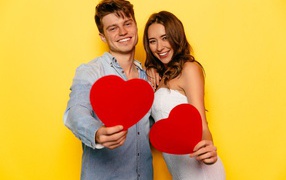 Влюбленная пара на желтом фоне с бумажными сердечками в руках 