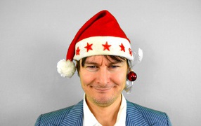 Голубоглазый мужчина в новогодней шапке на сером фоне 