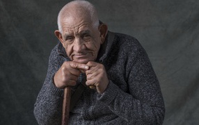 Пожилой мужчина в теплом свитере на сером фоне 