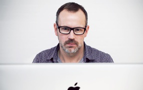Серьезный мужчина в очках сидит за макбуком