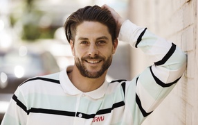 Улыбающийся мужчина в рубашке стоит у стены