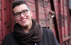 Улыбающийся мужчина в очках у стены 