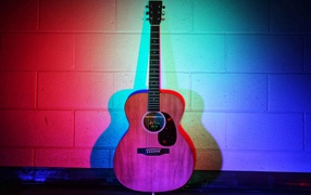 The guitar stands against the wall in a multicolored light