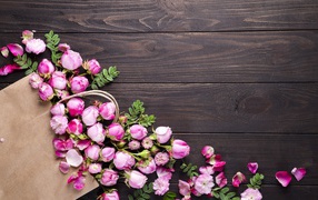 Цветки розовой розы с бумажным пакетом  на деревянном фоне