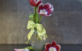 Три розовых цветка тюльпана в стеклянной вазе у стены