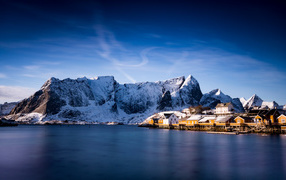 Красивый вид на дома у заснеженных гор под голубым небом 