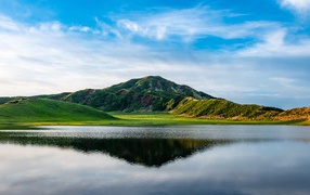 Красивый вид на покрытую зеленью гору под голубым небом у озера